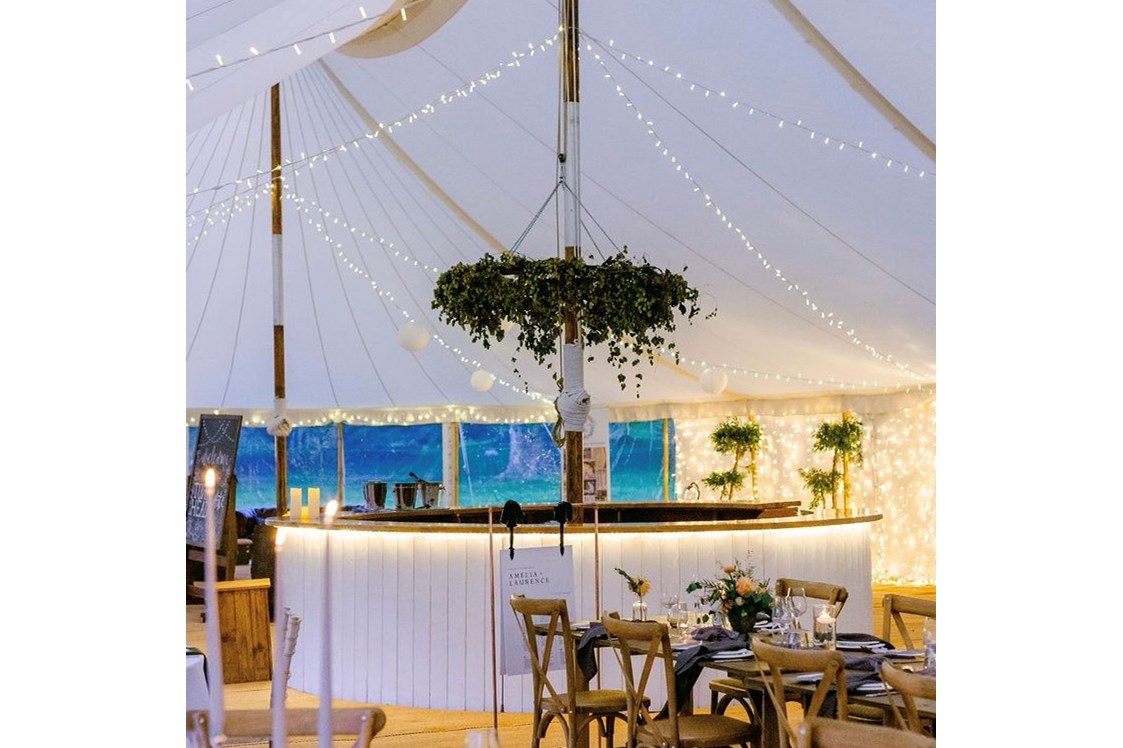 Hochzeit: Die Bar aus Eichenholz gibt es je nach Größe des gewählten Zeltes entweder rund oder halbrund. Hier seht Ihr die runde Bar mit einem schwebenden Blumenkranz.  - Schloss Jeutendorf Marquees