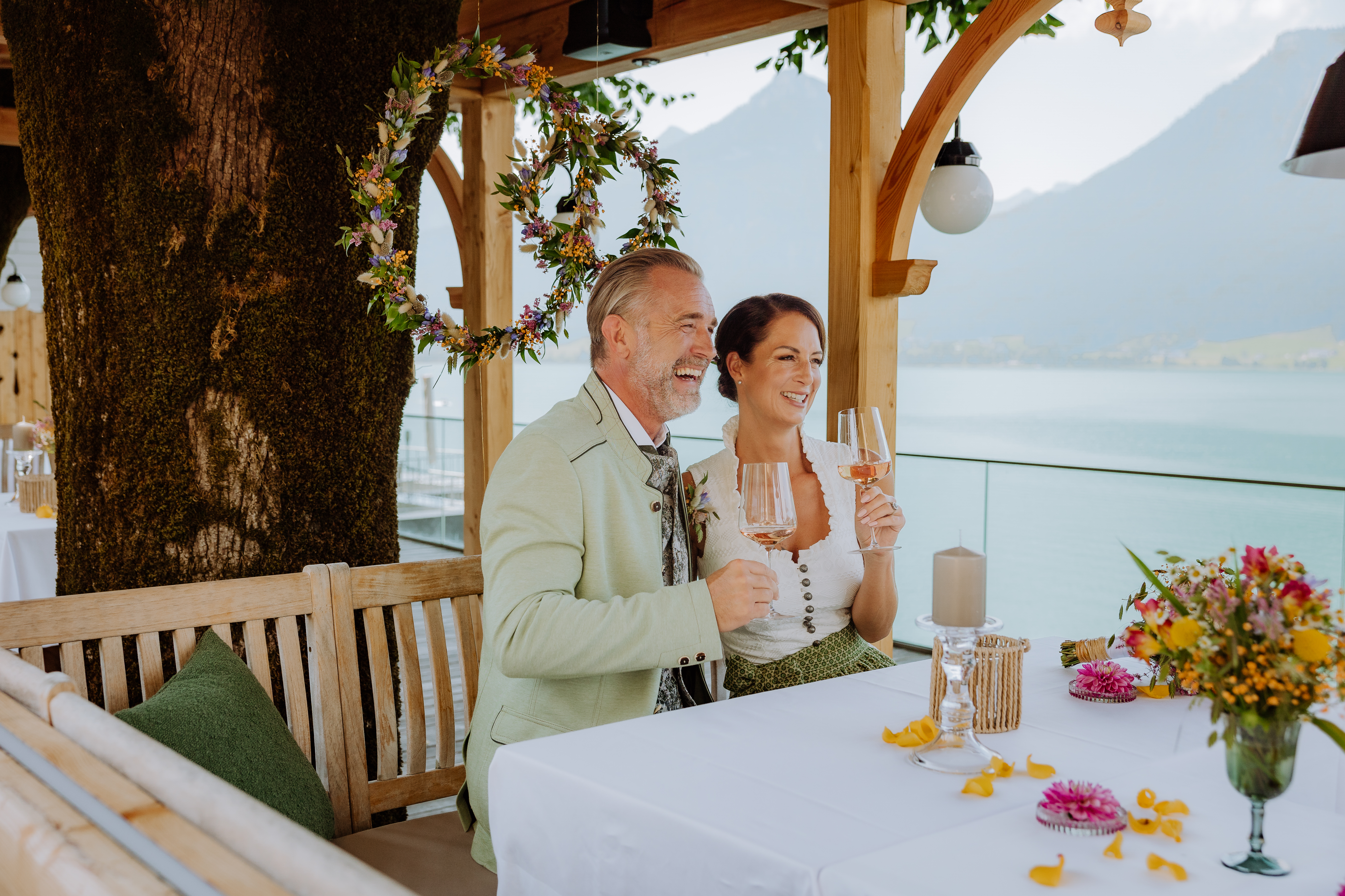 Hochzeit - Standesamt - Salzkammergut - Hochzeitspaar in der Hochzeitslocation Paul der Wirt. Das Paar sitzt unter einer Pergola mit Blick auf den Wolfgangsee. - Paul der Wirt, St. Wolfgang