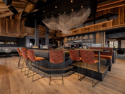 Mariage - Frühlingshochzeit - Unser Stolz: unsere kommunikative und große Bar, eingebettet in die Kombination von traditionellem Hüttenambiente mit viel Altholz und modernem Style. Sie lädt ein zum Verweilen mit Freunden, zum gemeinsamen Drink während der Partynacht oder einfach zum Genießen der wunderschönen Aussicht. Highlight ist unser Kristall-Adler, welcher für ein besonderes Ambiente sorgt und abends unser Restaurant in ein besonderes Licht verzaubert. - jezz AlmResort Ellmau