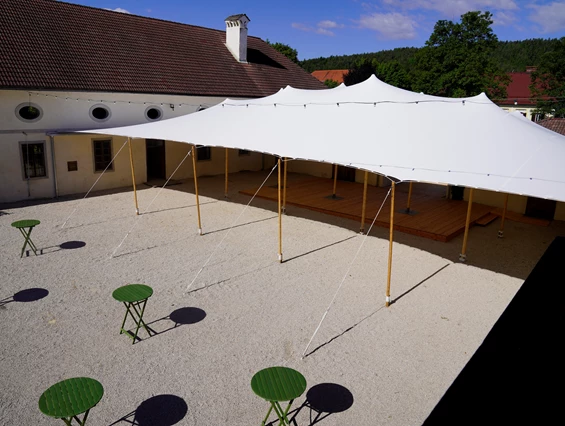 Hochzeit: Innenhof der Alten Meierei Bleiburg mit weißem Festzelt / Zeltüberdachung ohne Seitenwände und grünen Stehtischen. - ALTE MEIEREI BLEIBURG