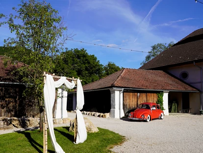 Hochzeit - PLZ 9155 (Österreich) - Roter VW Käfer und Brautbogen im Innenhof der Alten Meierei Bleiburg - ALTE MEIEREI BLEIBURG