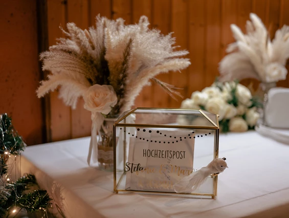 Hochzeitslocation: Stilvolle Hochzeitspost-Box mit goldenen Details und Trockenblumen im Wanderheim Germersheim. Auf einem weißen Tisch im festlich geschmückten Saal bietet sie Platz für Glückwunschkarten und persönliche Nachrichten der Gäste. - Wanderheim Germersheim
