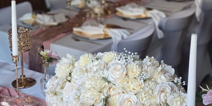 Bruiloft - Wiesloch - Blick vom Brauttisch im festlich geschmückten Saal des Wanderheim Germersheim. Ein üppiges Blumengesteck aus weißen und cremefarbenen Rosen ziert den Tisch, ergänzt durch goldene Kerzenhalter und roségoldene Akzente. Die harmonische Kombination aus Farben und Licht verleiht der Hochzeitsdekoration eine luxuriöse, zugleich warme Atmosphäre – ideal für stilvolle Feiern in der Pfalz. - Wanderheim Germersheim