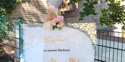 Bruiloft - Wiesloch - Ein liebevoll gestaltetes Willkommensschild auf einer Staffelei begrüßt die Gäste am Eingang des Wanderheim Germersheim. Umrahmt von floraler Dekoration und sanftem Licht vermittelt es sofort festliche Stimmung und persönliche Note.  - Wanderheim Germersheim