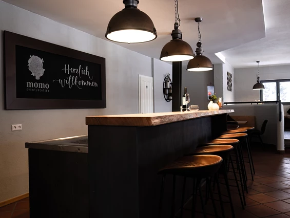 Hochzeitslocation: Eingangsbereich: Theke mit integrierten Kühlschränken mit Tresen, Barhockern und Tafel - momo Eventlocation