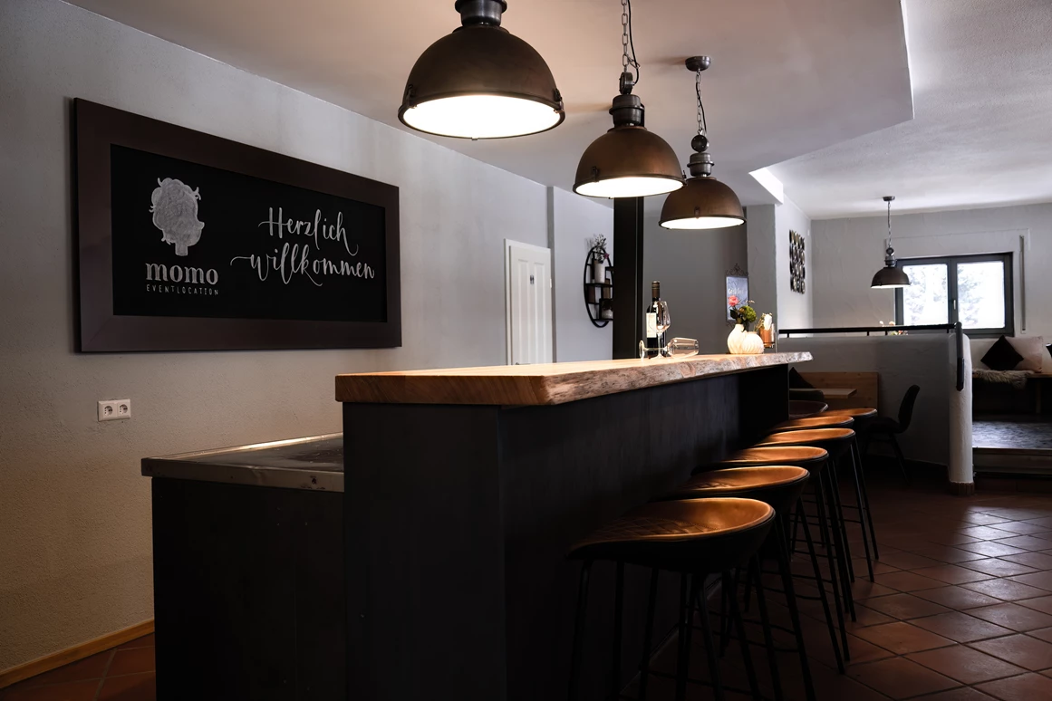 Hochzeitslocation: Eingangsbereich: Theke mit integrierten Kühlschränken mit Tresen, Barhockern und Tafel - momo Eventlocation