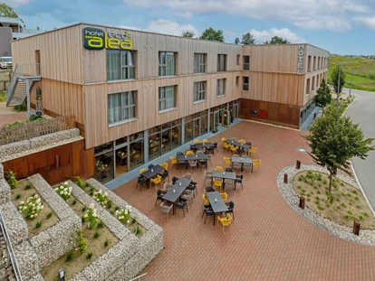 Matrimonio - Haag an der Amper - Das Alea- Eco finden Sie im Pfaffenhofener Eco-Quartier, einem Stadtteil mit strikt ökologischer Ausrichtung. Eine tolle Gelegenheit für Urlauber oder Geschäftsleute - mit dem ökologischen Herz am rechten Fleck - sich hier wohlzufühlen.
Es dominiert Holz als Baustoff, die Heizung und der verbrauchte Strom sind nahezu CO2 neutral. Die Photovoltaik-Anlage auf der großen Dachfläche kann im Vollausbau mehr Strom erzeugen als verbraucht wird. Es wird auf Abfallvermeidung gesetzt.
Das galt für die Wärmedämmung ohne Kunststoff ebenso wie beim Mobiliar und natürlich die Gastronomie: Wenn wir Kunststoffe einsetzen, dann sollten sie aus Recyclingprozessen stammen.
Dass im Hotel-Betrieb regional und, soweit möglich, biologisch zertifizierte Produkte eingekauft werden, versteht sich dabei von selbst. Da ist vieles möglich, sogar für Reis aus dem Landkreis Pfaffenhofen haben wir einen Lieferanten - Hotel Alea Eco